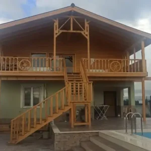 Hafif bulutlu havada çekilmiş beton tuğla üzeri büyük geniş ahşap merdiven ile çıkılan ahşap kütük ev görseli