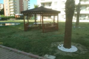 Palmiye ağaçları arasında yerleri çim olan bahçede konumlandırılmış altıgen kamelya görseli