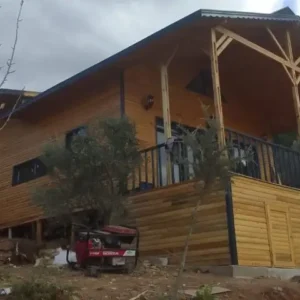 Hafif bulutlu havada çekilmiş veranda ve yan boyu gösteren sürdürülebilir ahşap ev projesi görseli