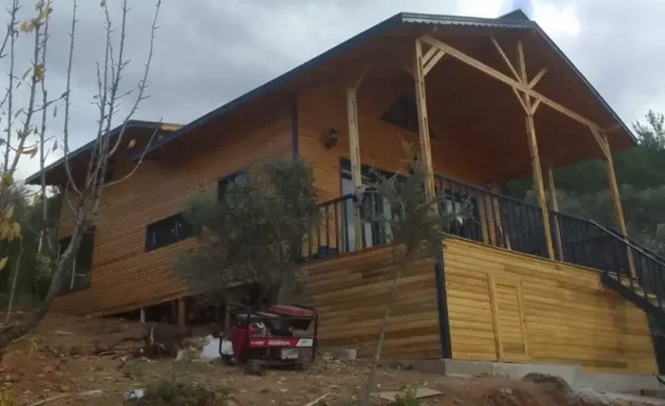 Hafif bulutlu havada çekilmiş veranda ve yan boyu gösteren sürdürülebilir ahşap ev projesi görseli