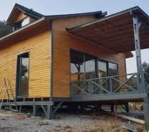 Vernadadan çekilmiş büyük cam kapılı çatısında kuş gözü olan ahşap ev