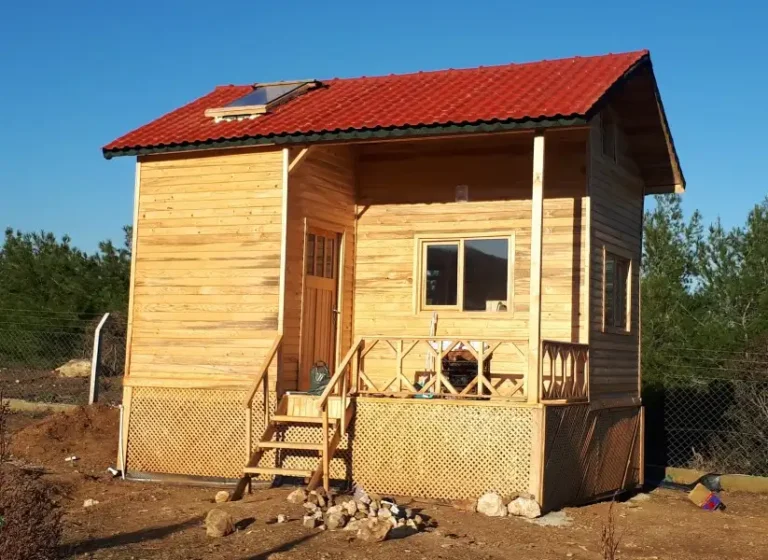 Kırmızı çatısı olan önünde verandası ile iki katlı küçük 20 m2 bungalov ev