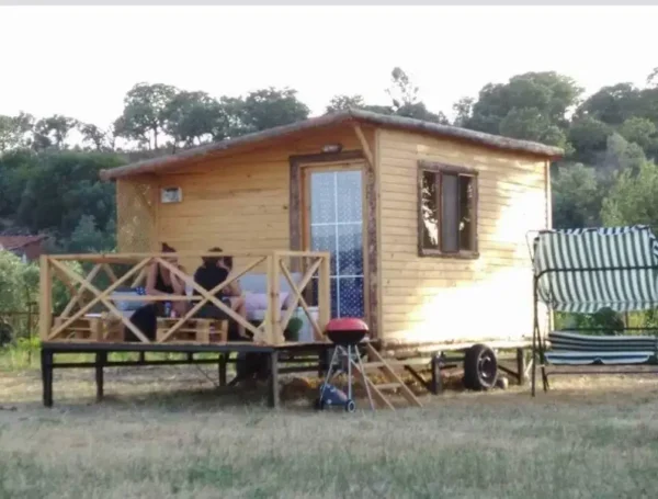 Ağaçlar içinde mangal ve verandasında oturan üç bayanı olan ahşap karavan