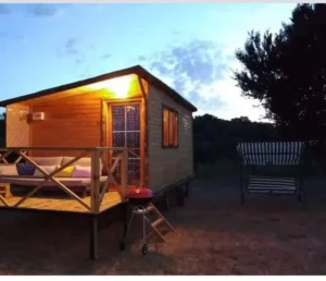 Hafif güneş batarken çekilmiş verandasının ışığı yanan ahşap karavan modelleri görseli