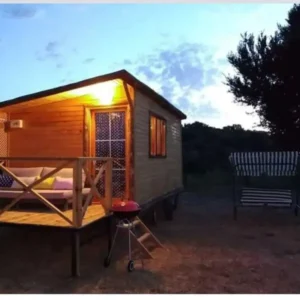 Hafif güneş batarken çekilmiş verandasının ışığı yanan ahşap karavan modelleri görseli