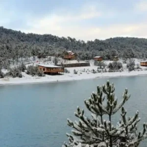 Karlarla kaplı orman ve göl manzarası arasında ahşap kafe restaurant tesisi