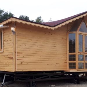 Adanın üzerinde yerler toprak zemin ve arkası ağaçlık alanda konumlanmış önü camekan ve giriş bölümü korunaklı 2+1 Tiny House fiyatları görseli