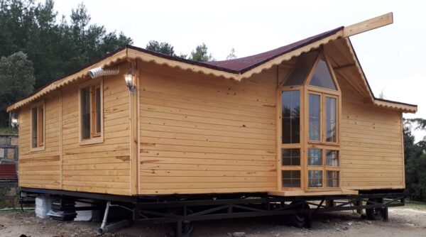 Adanın üzerinde yerler toprak zemin ve arkası ağaçlık alanda konumlanmış önü camekan ve giriş bölümü korunaklı 2+1 Tiny House fiyatları görseli